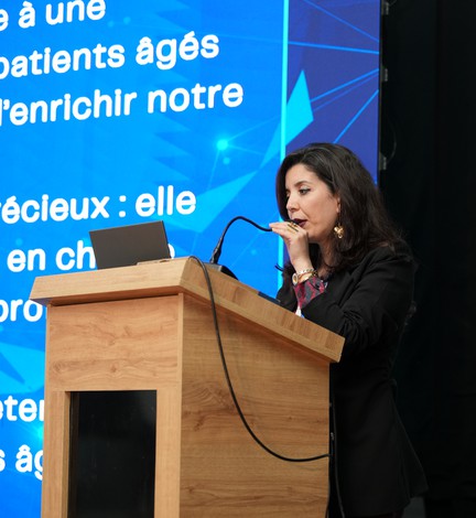 Une intervenante au pupitre devant un écran de présentation